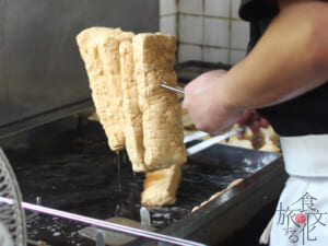 揚がったあぶらげを金串に差して油切りする